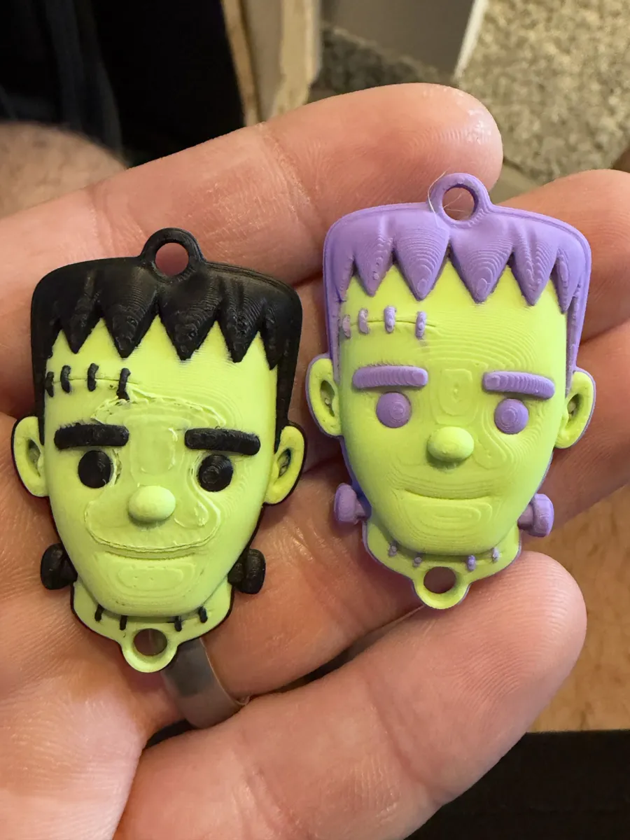 Two Frankenstein charms, one black and green, one purple and green
